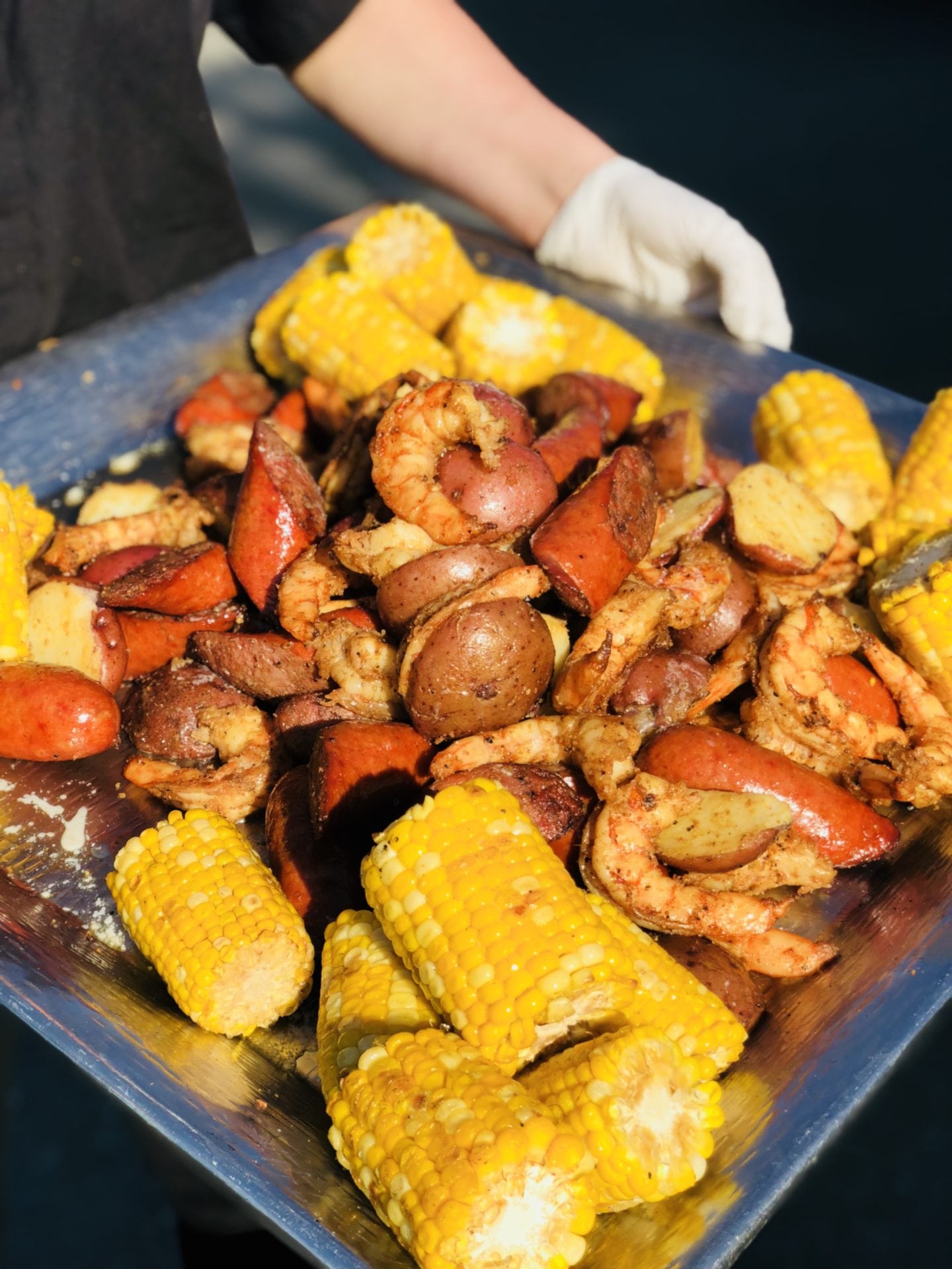A plate of food with shrimp, corn and sausage.