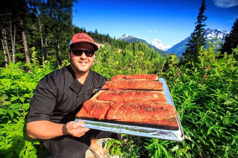 A man holding a tray of meat in front of some trees.