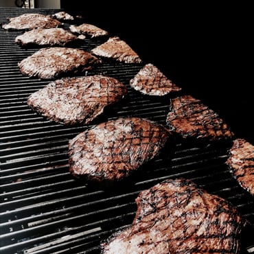 A lot of pieces of meat on the grill with a black background